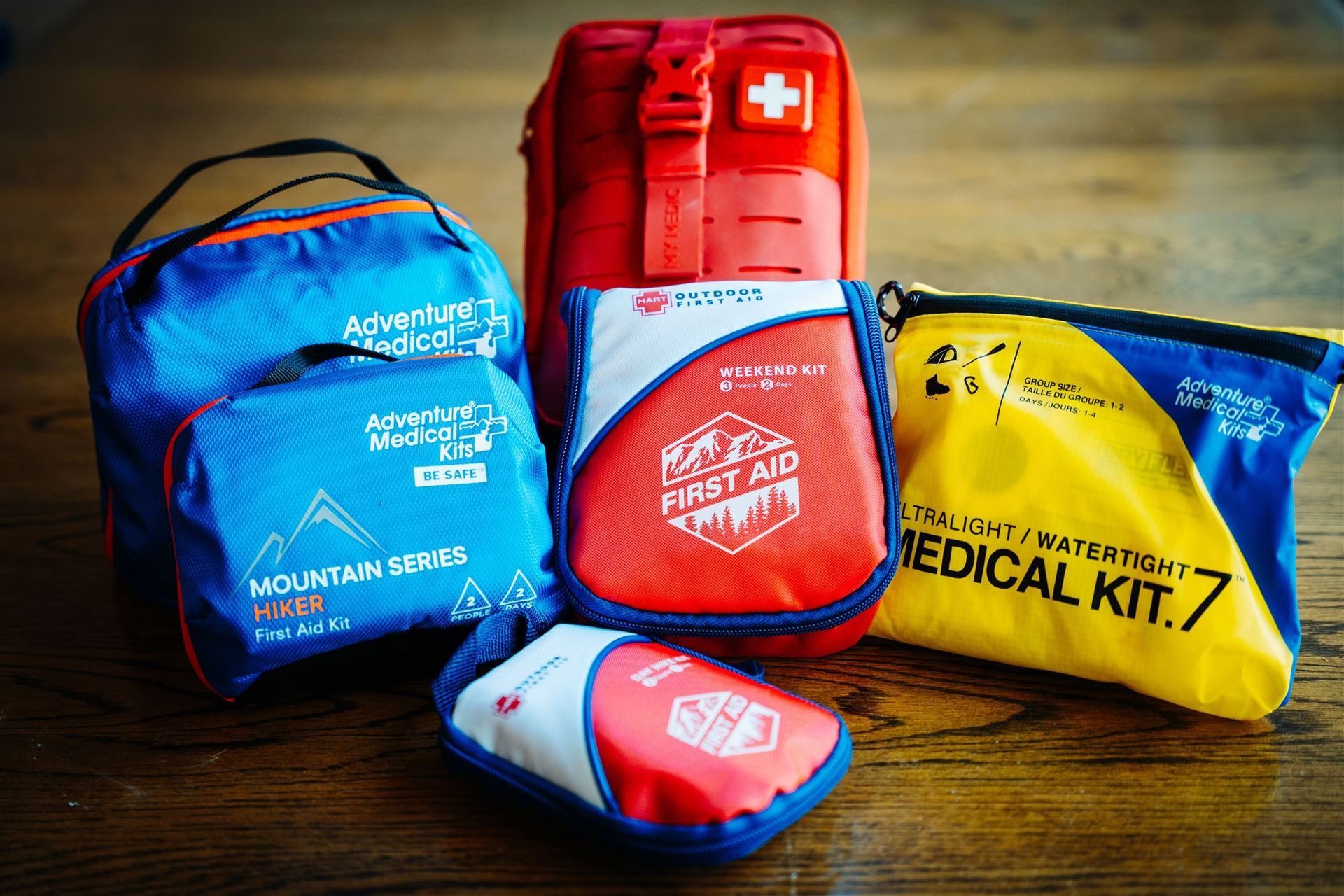 Four colorful emergency medical kits on a wooden table, including blue, red, and yellow zippered pouches