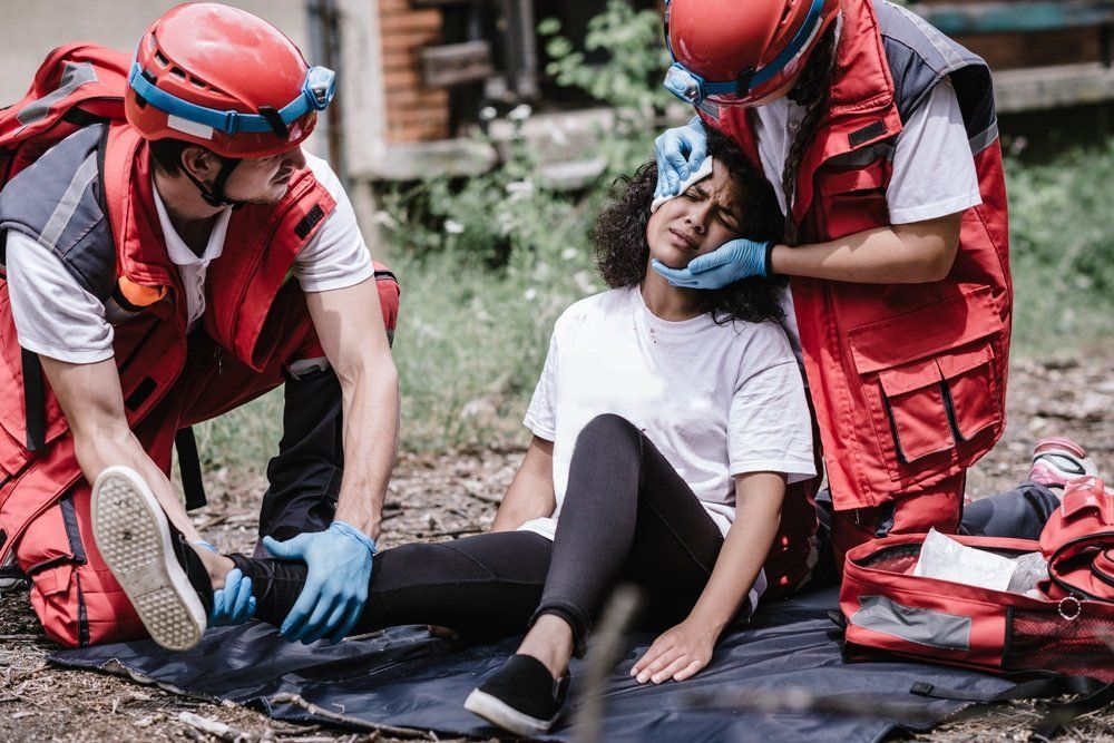 Two paramedics assisting an injured person seated on the ground outdoors
