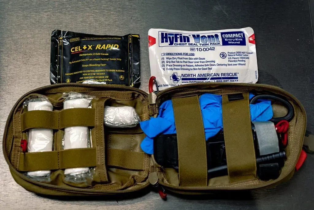 Open first aid kit with medical supplies, gauze, gloves, and black elastic straps on a gray surface