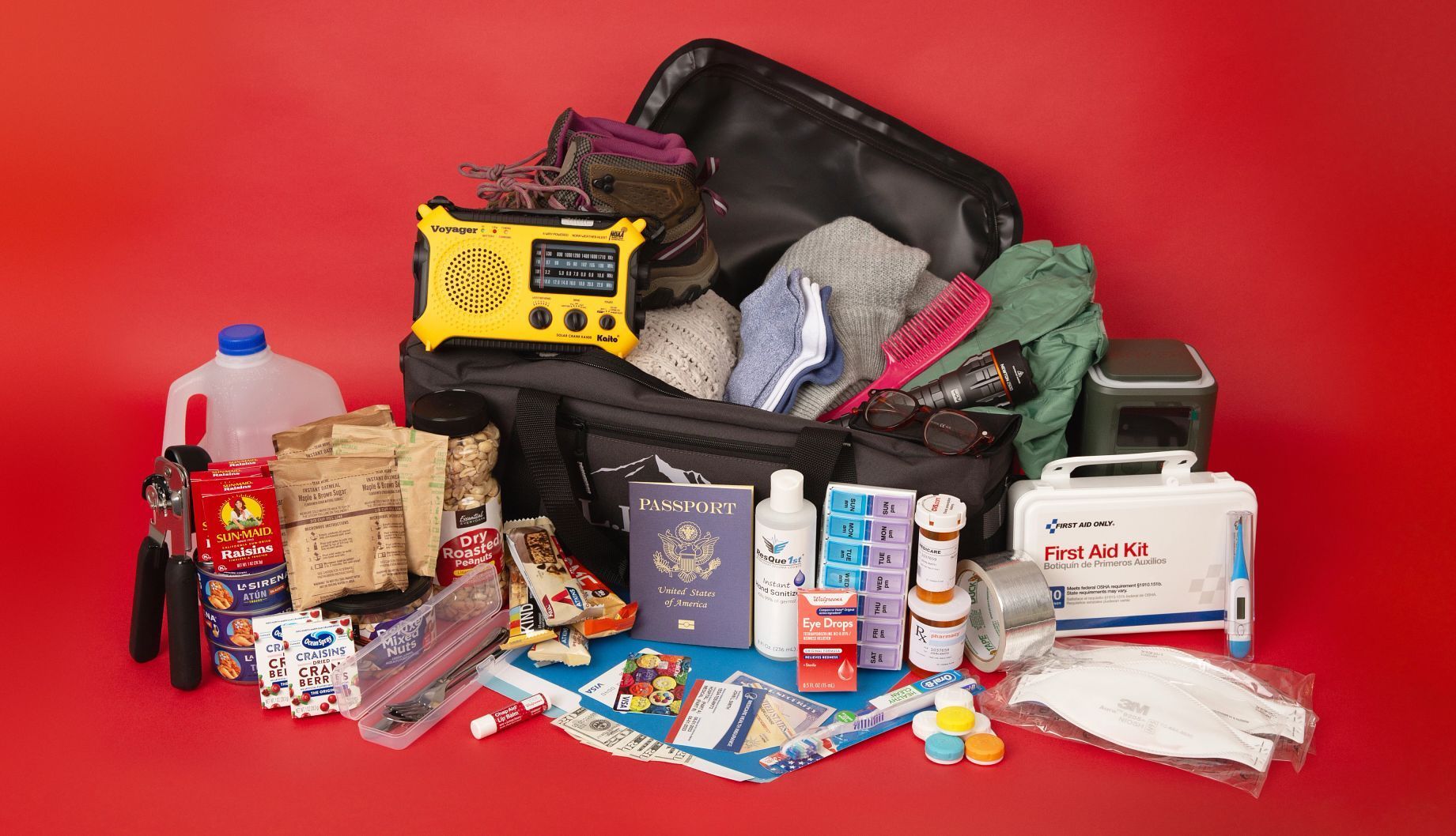 Travel suitcase open on red background, surrounded by assorted toiletries, snacks, and travel essentials