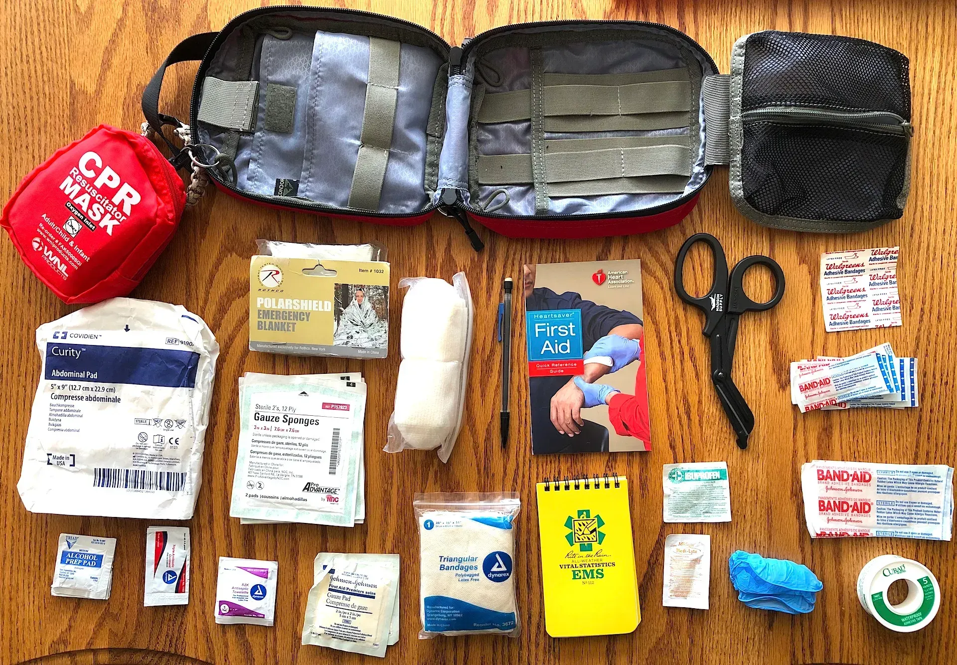 Assorted first-aid and toiletry supplies neatly arranged on a wooden floor, including bags, bandages, scissors, and tape