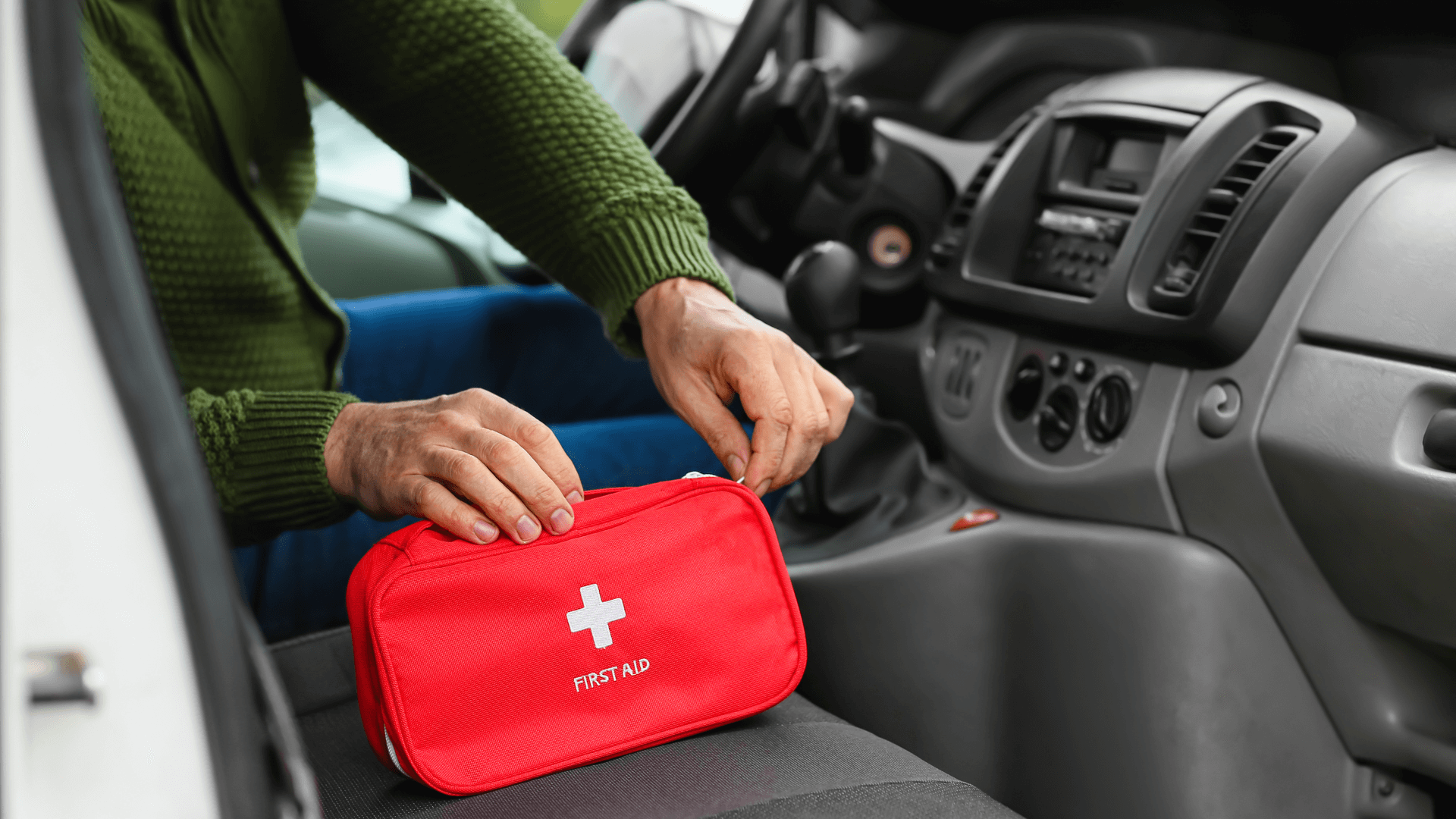 Person placing a red first aid kit on a car seat inside a vehicle