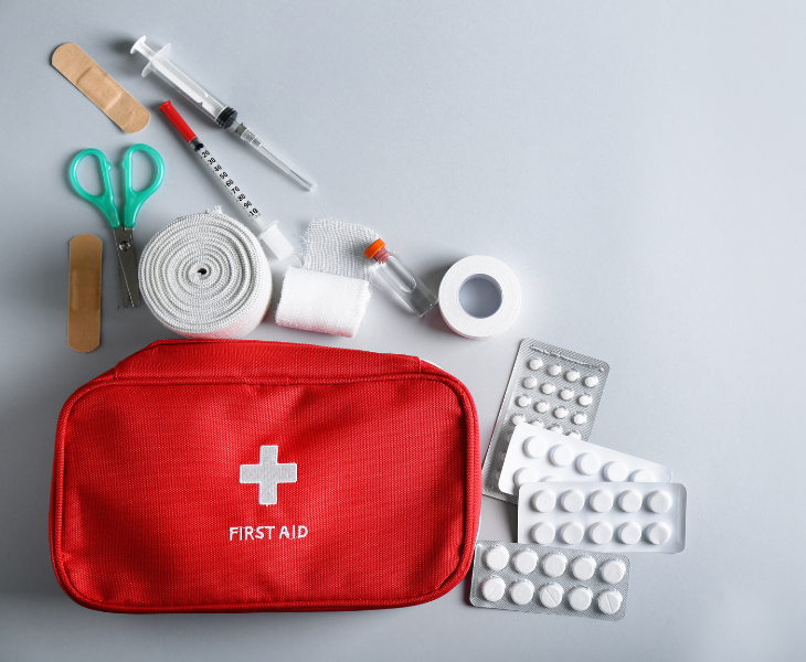 Red first aid kit with bandages, scissors, tape, and pills on a light background