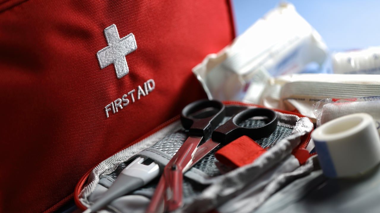 Red first aid kit with white cross and medical supplies, including scissors, bandage, and gauze
