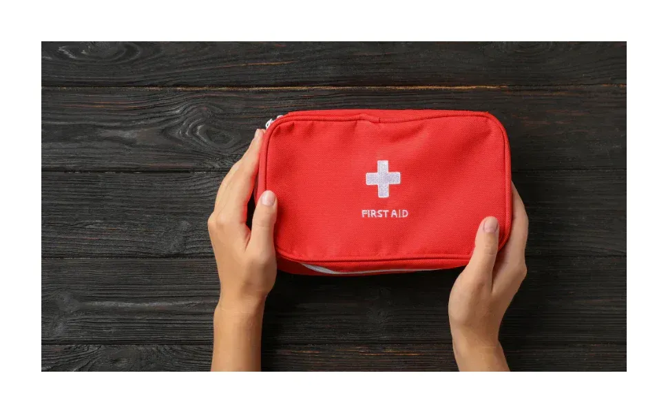 Red first aid kit with white cross held on a dark wooden surface