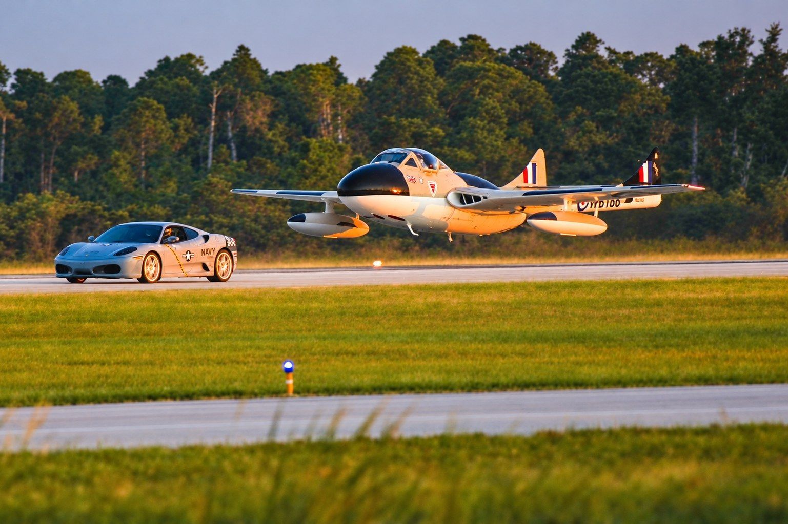 Precision Exotics sports car racing alongside a low-flying vintage jet on the runway at the Florida 
