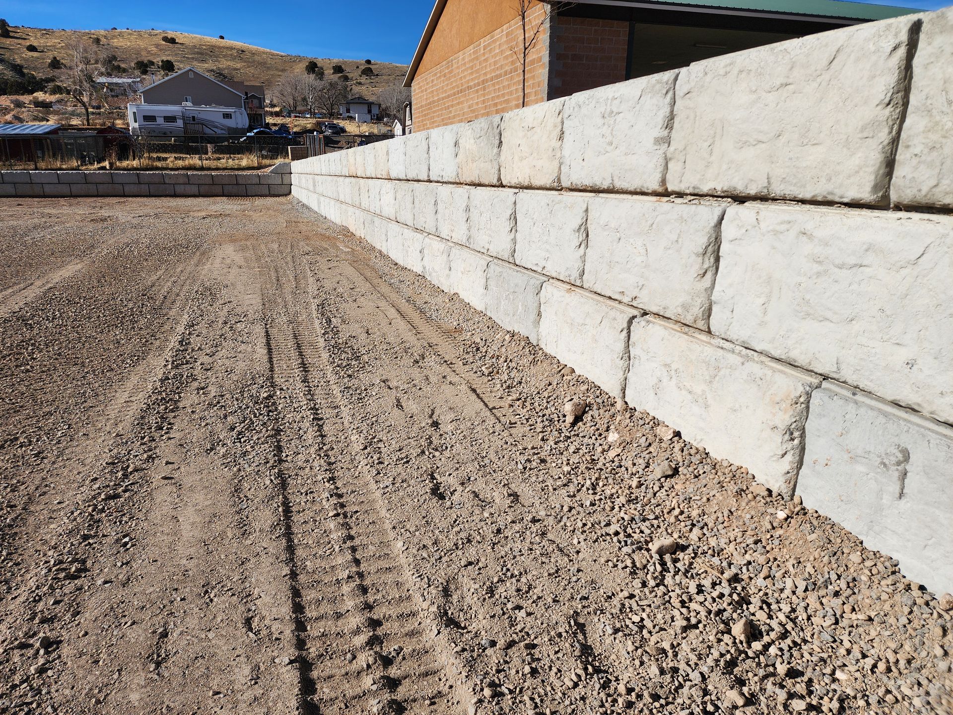 Dirt lot beside a white block retaining wall under a clear blue sky