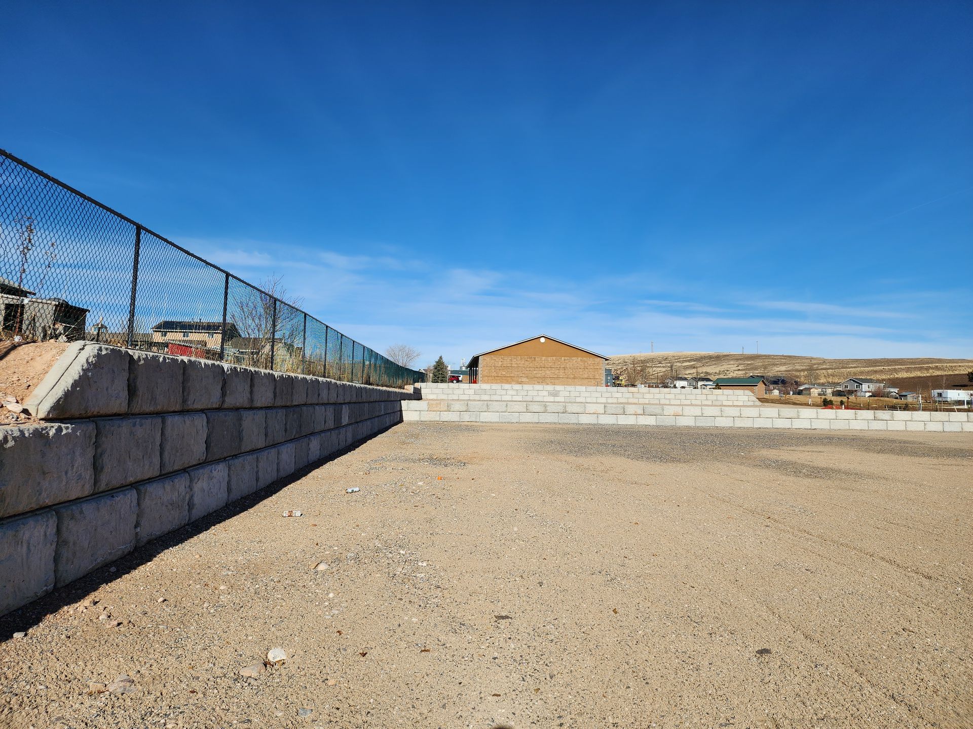 Empty gravel lot beside a chain-link fence under a clear blue sky