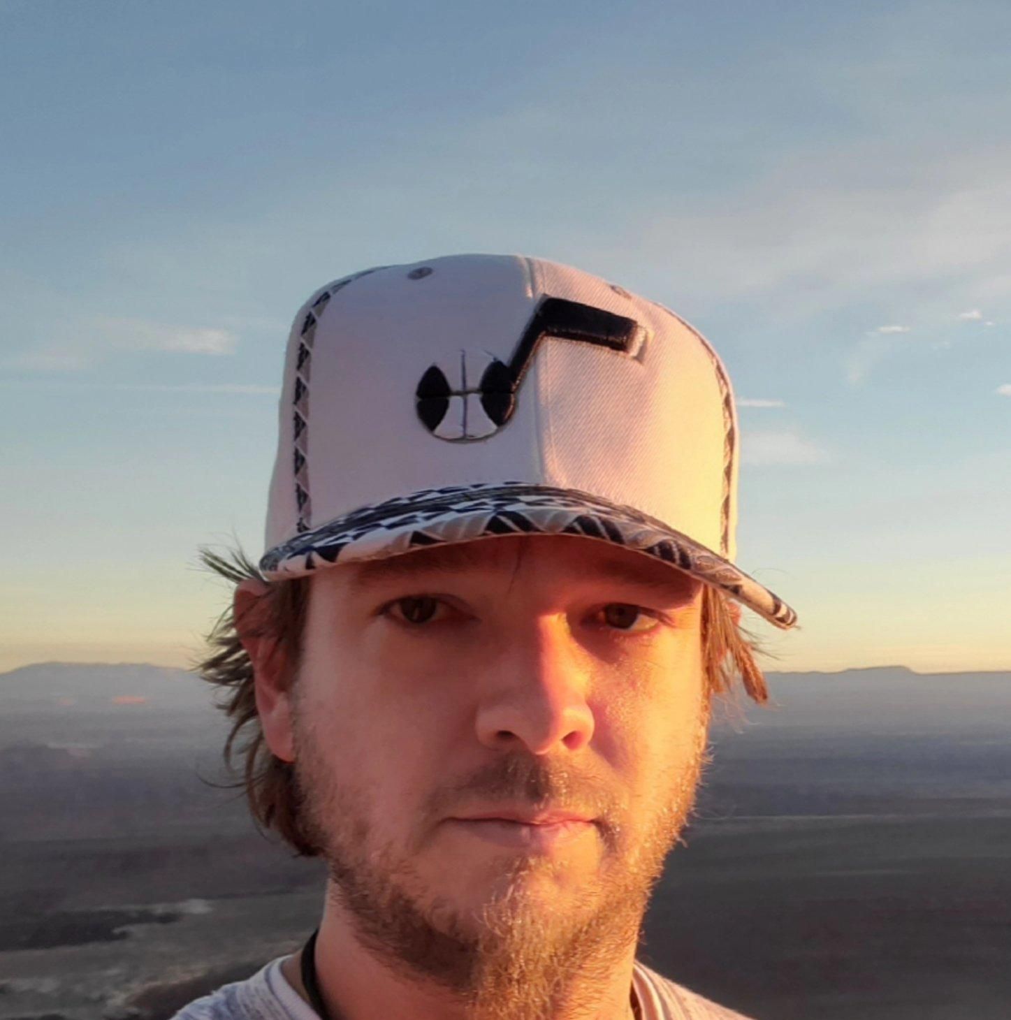Close-up of a person wearing a white patterned cap at sunset with mountains in the background