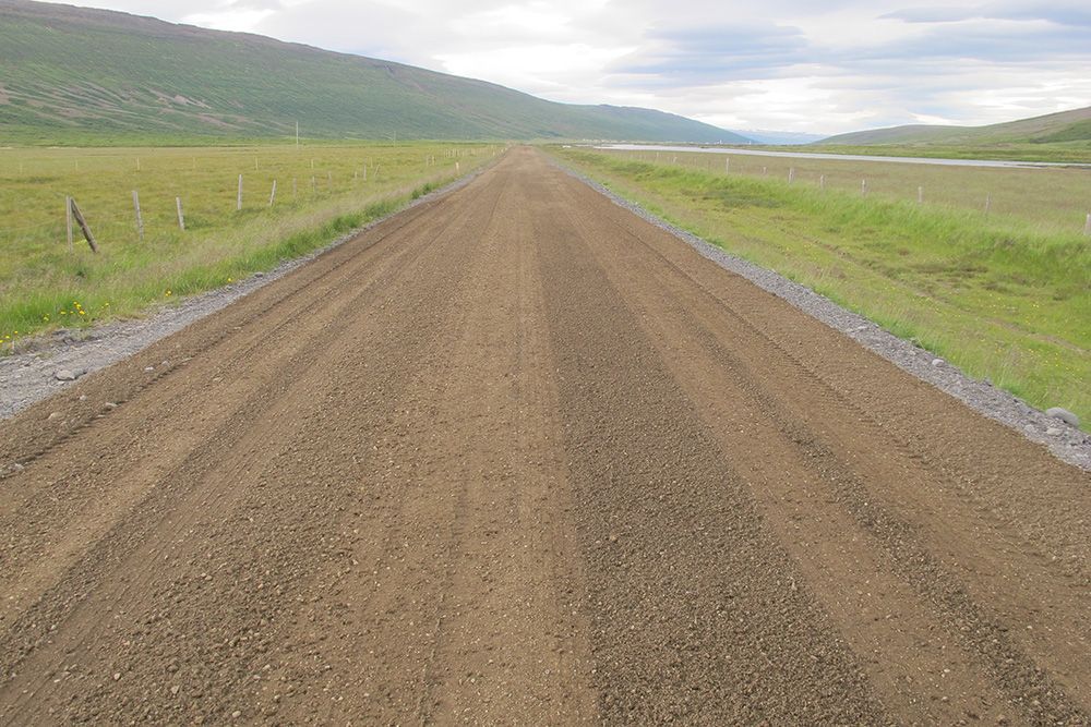 Gravel road stretching through open green hills under a cloudy sky
