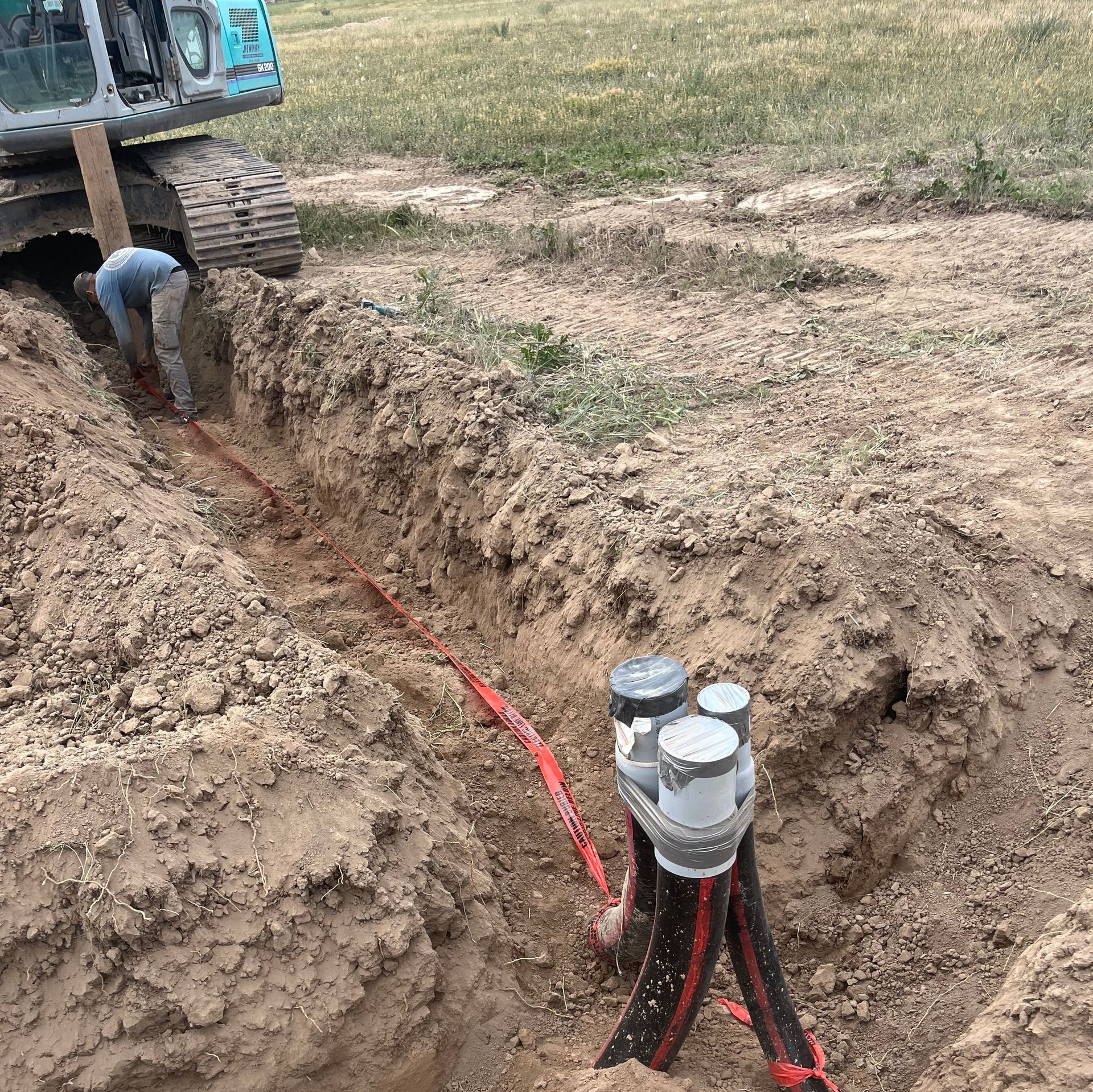 Trench with red cables and gray utility box beside a small excavator in a dirt field