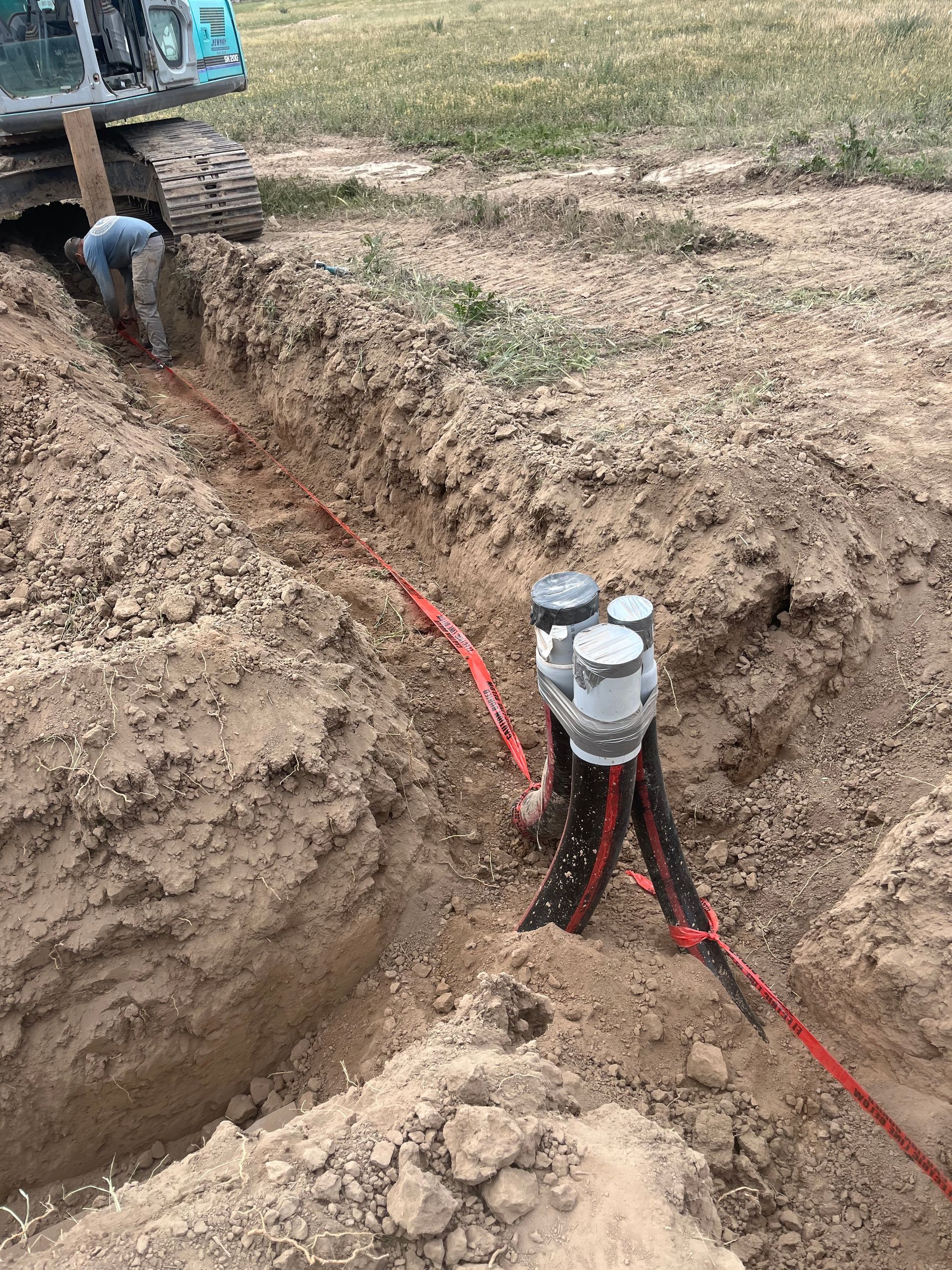 Utility trench with red cables and a gray pipe fitting in an excavated dirt field