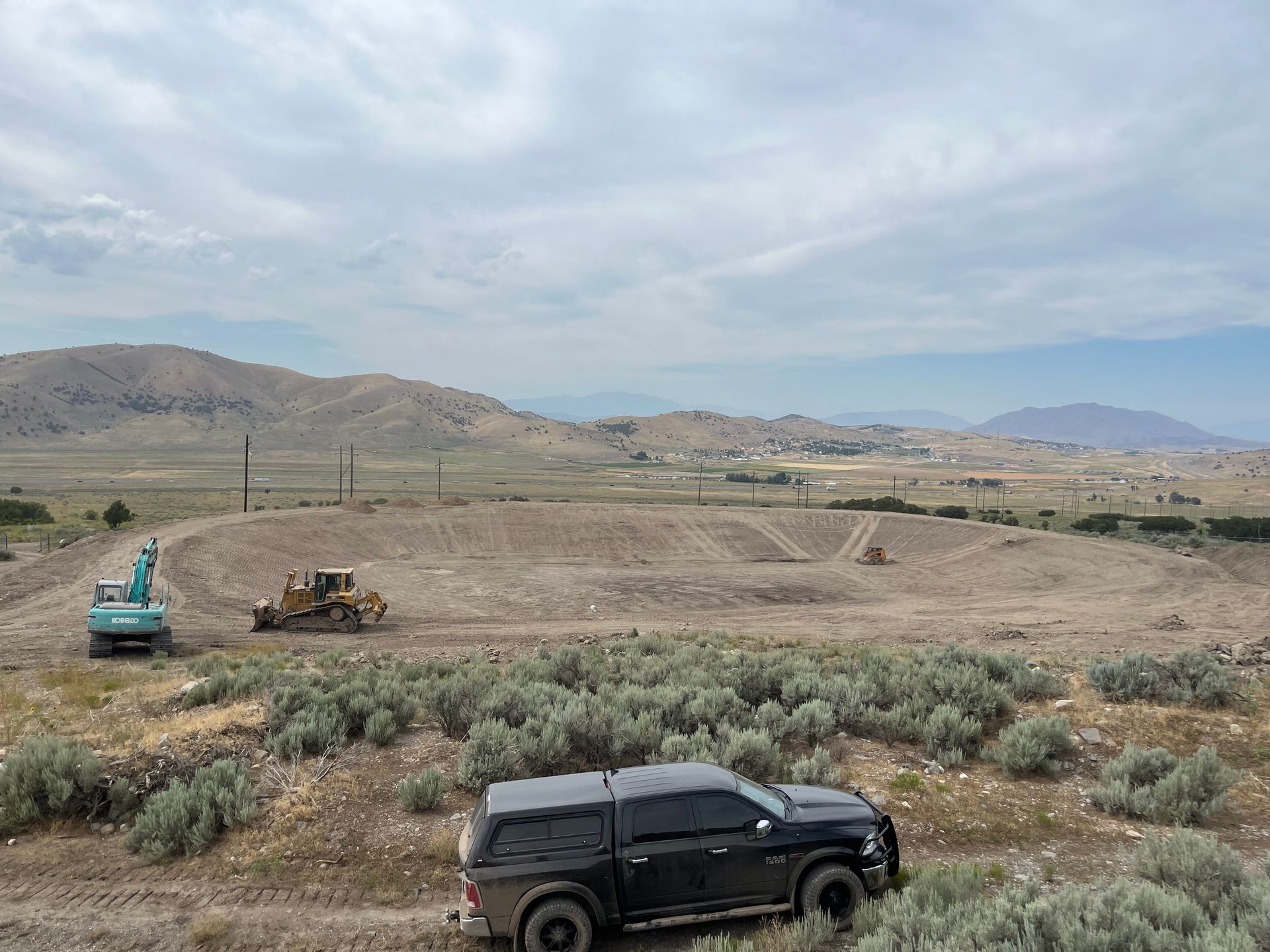 Black pickup overlooking a plowed field with heavy machinery and mountains in the distance