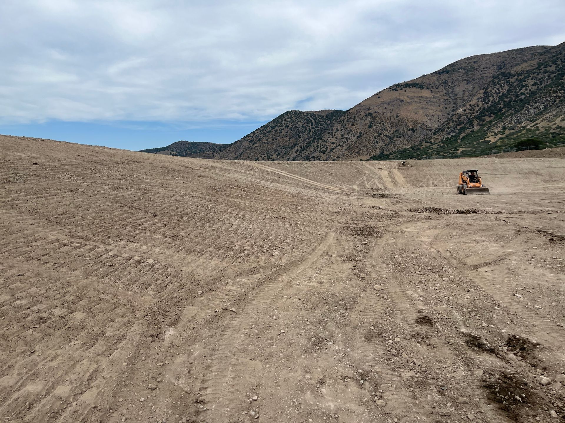 Wide sandy desert landscape with an off-road vehicle driving near rocky hills under a cloudy sky