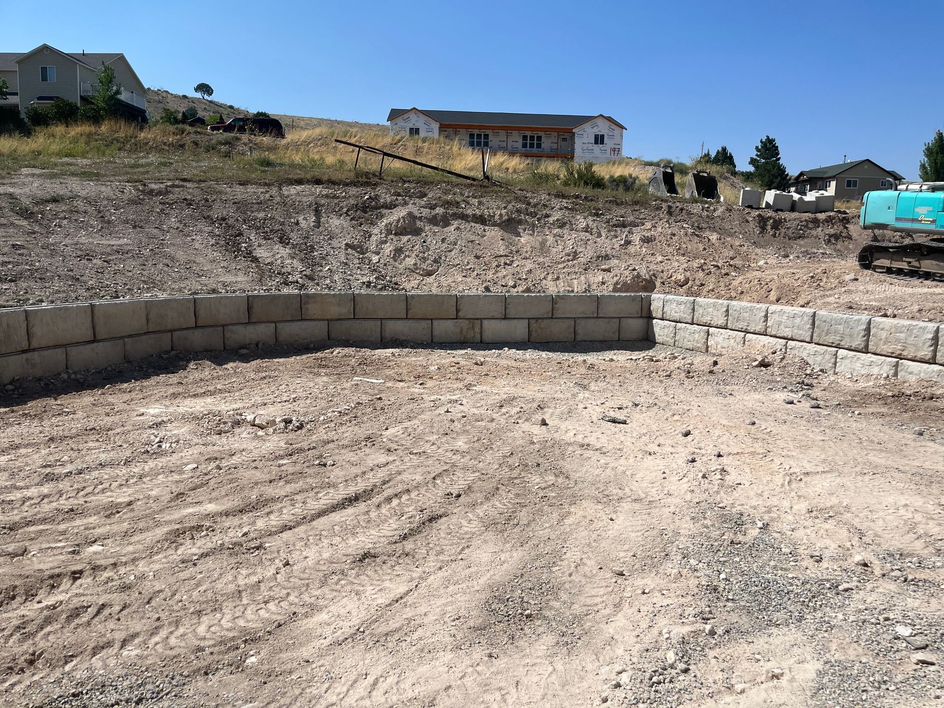 Retaining wall built on a dirt lot with houses on a hillside in the background