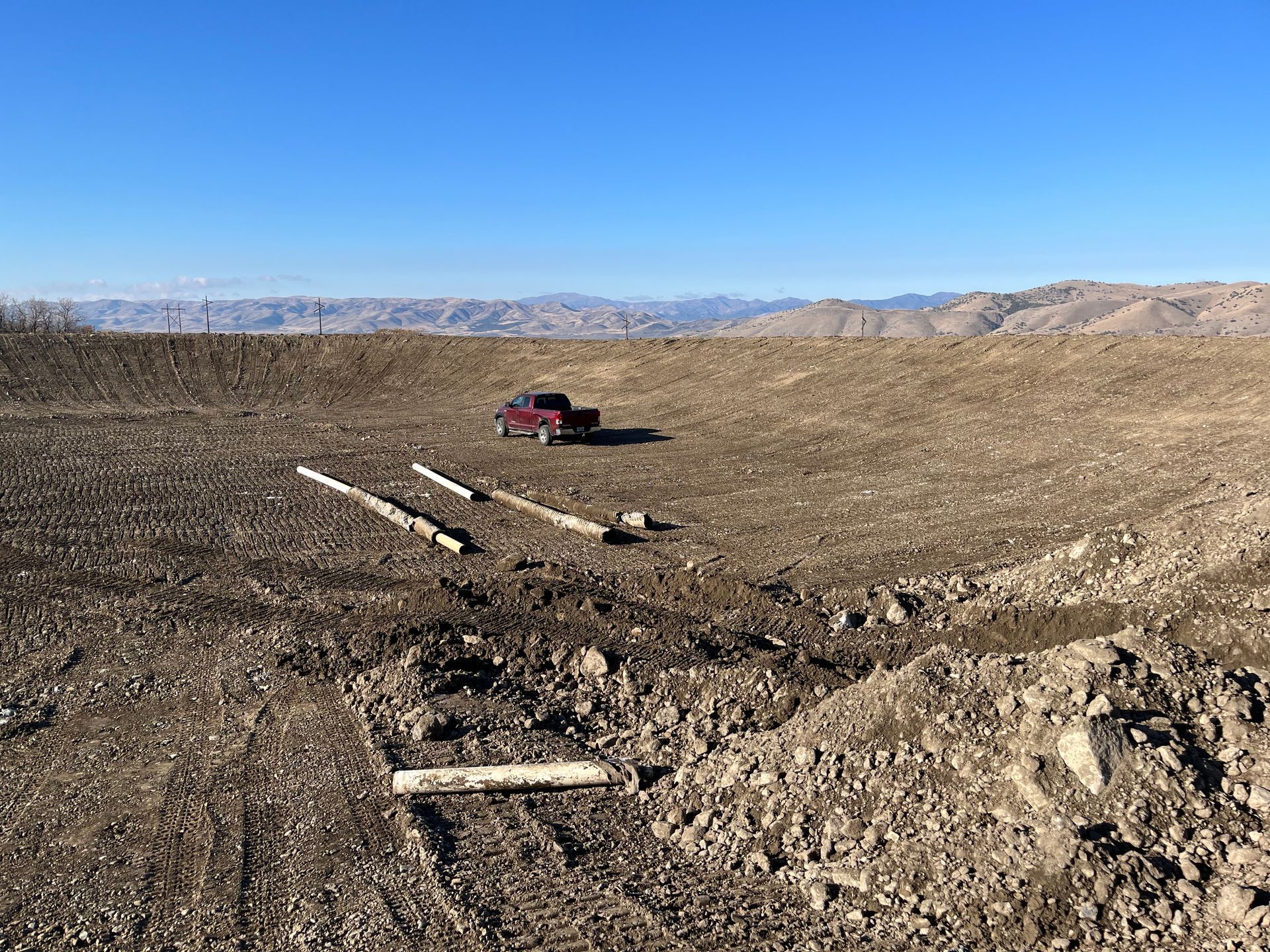 Red truck on a dirt road in a barren desert, with mountains under a clear blue sky.