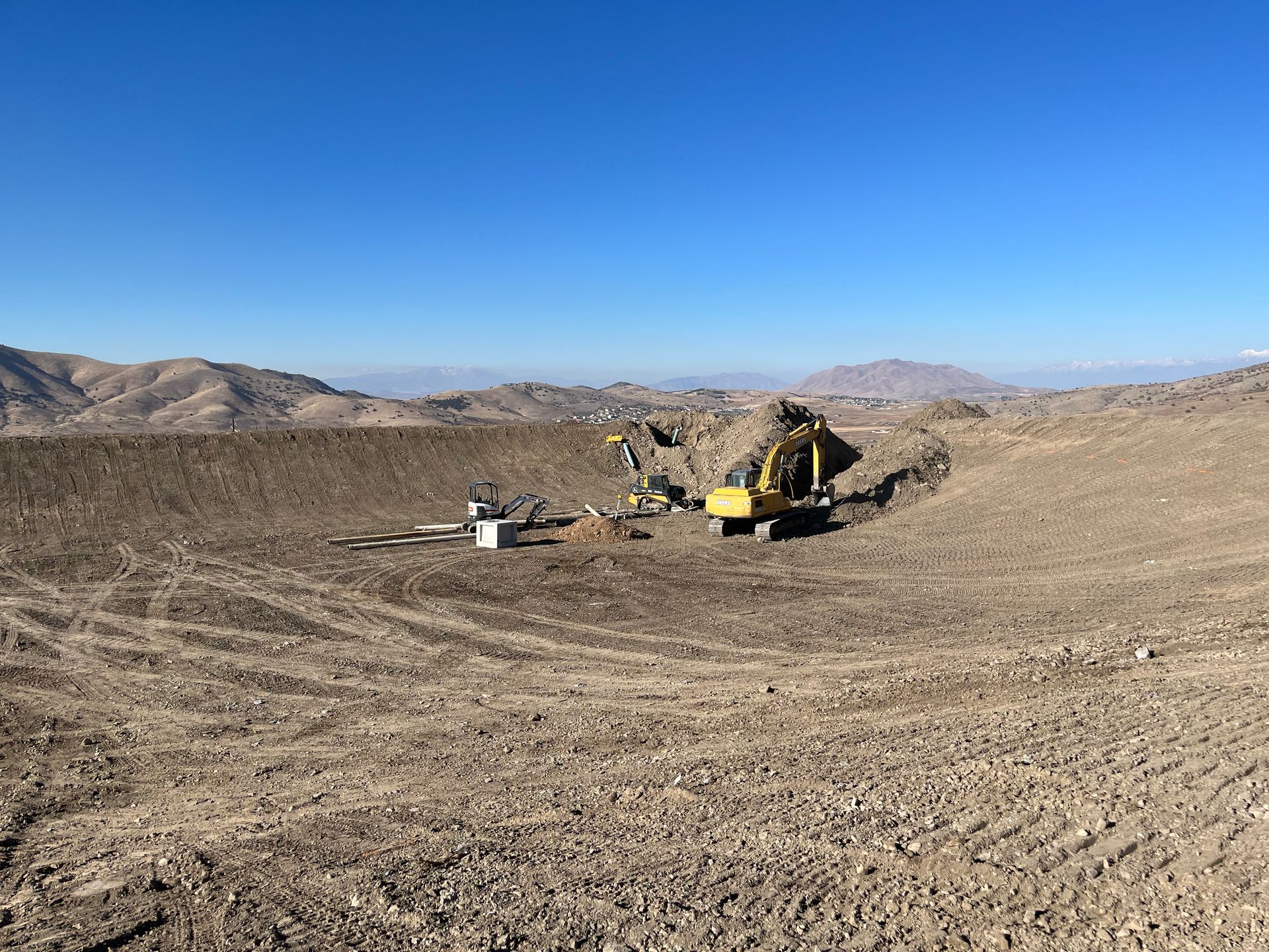 Excavator and dump truck working in a barren desert construction site under a clear blue sky