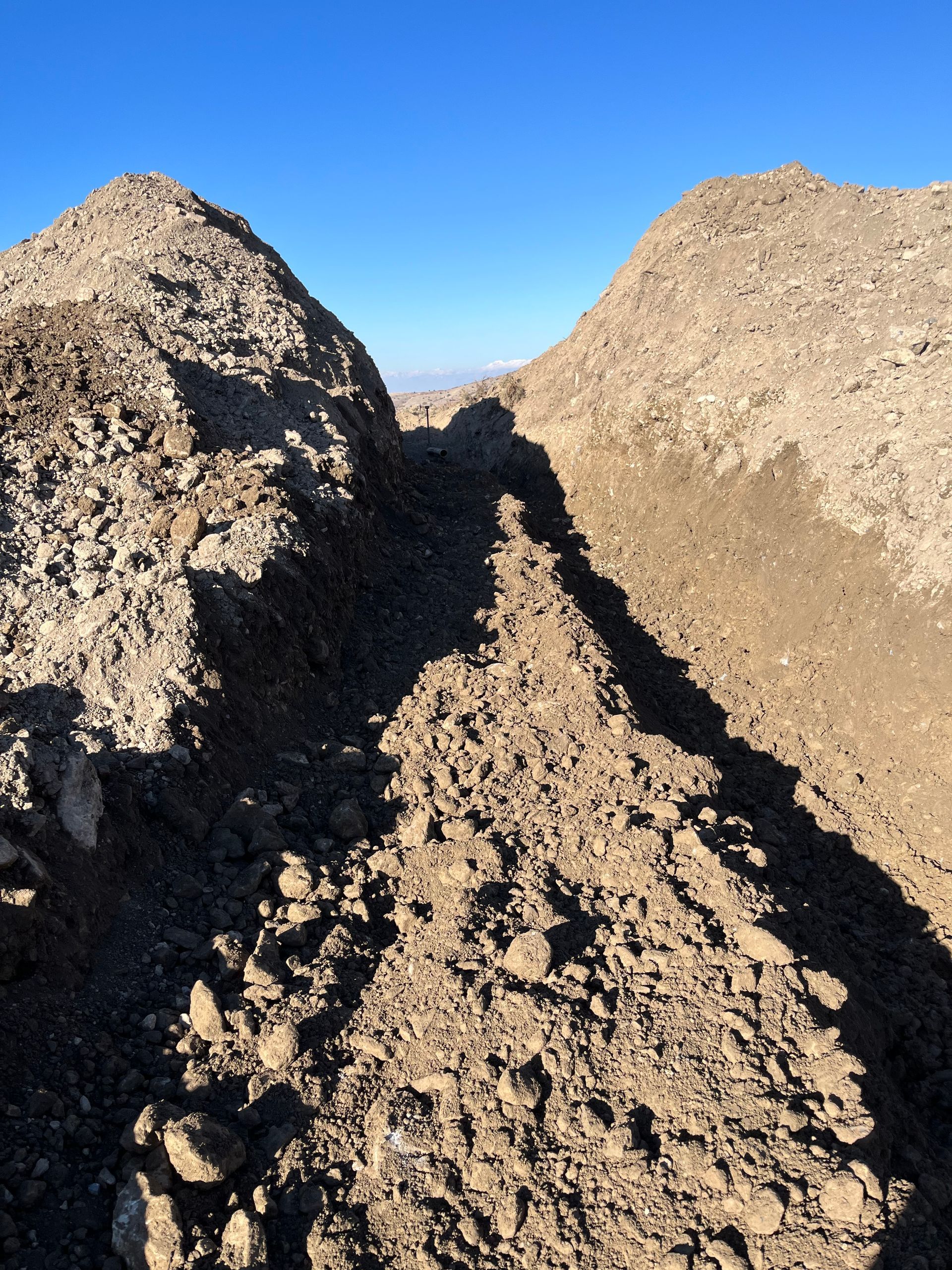 Large piles of dirt or gravel forming a rough trench under a clear blue sky.