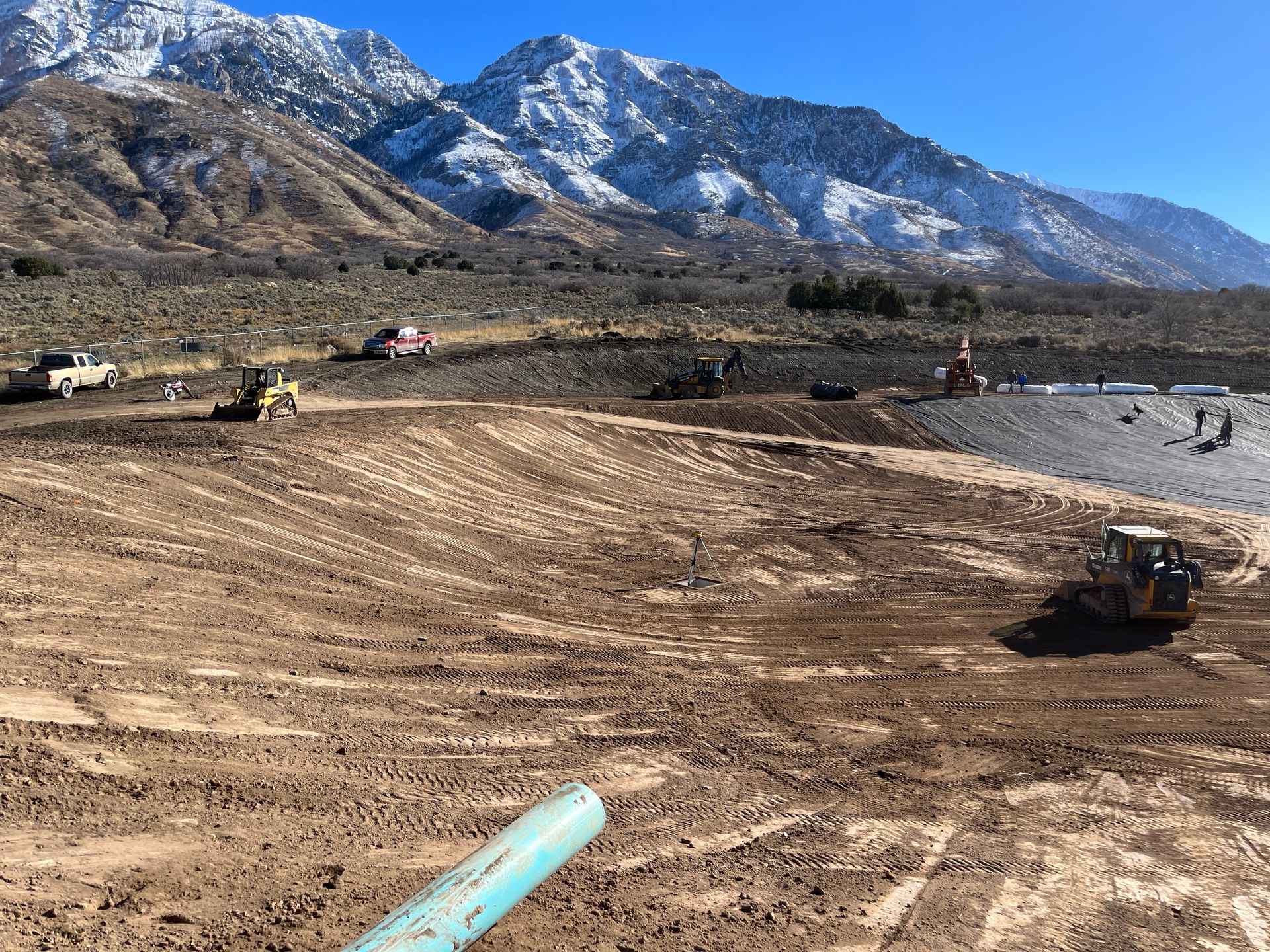 Construction site with heavy machinery on a dirt plain, mountains and snow in the background.