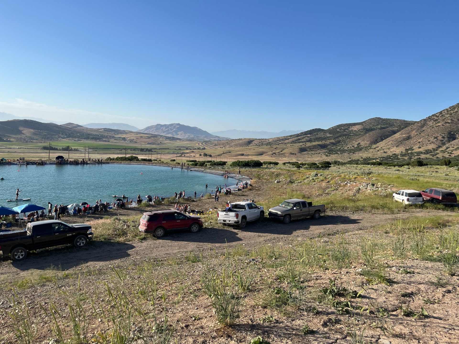 Parked cars beside a blue lake with hills and open sky in the background