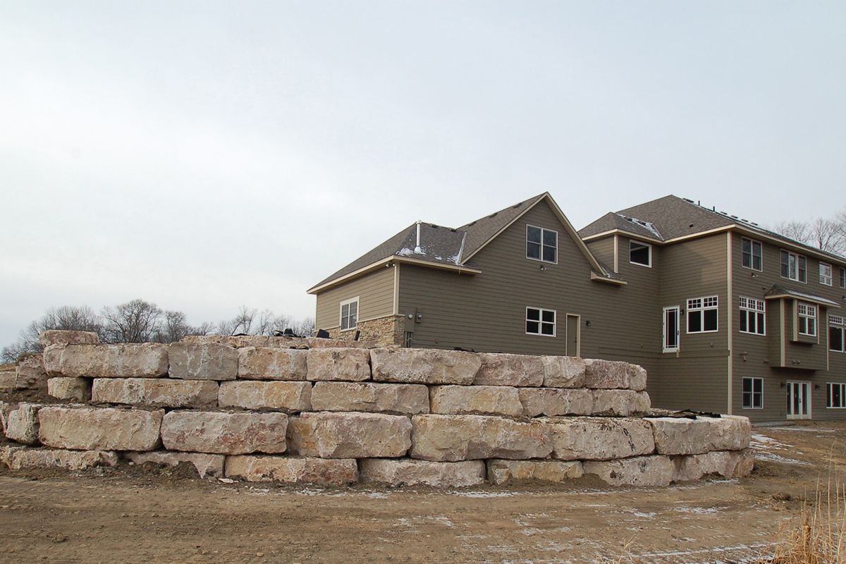 Stacked stone blocks in front of a beige apartment building under a cloudy sky