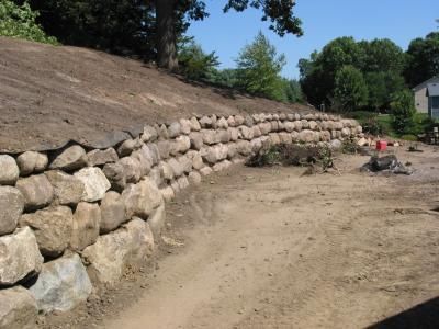 Stone retaining wall along a dirt path beside a hillside on a sunny day