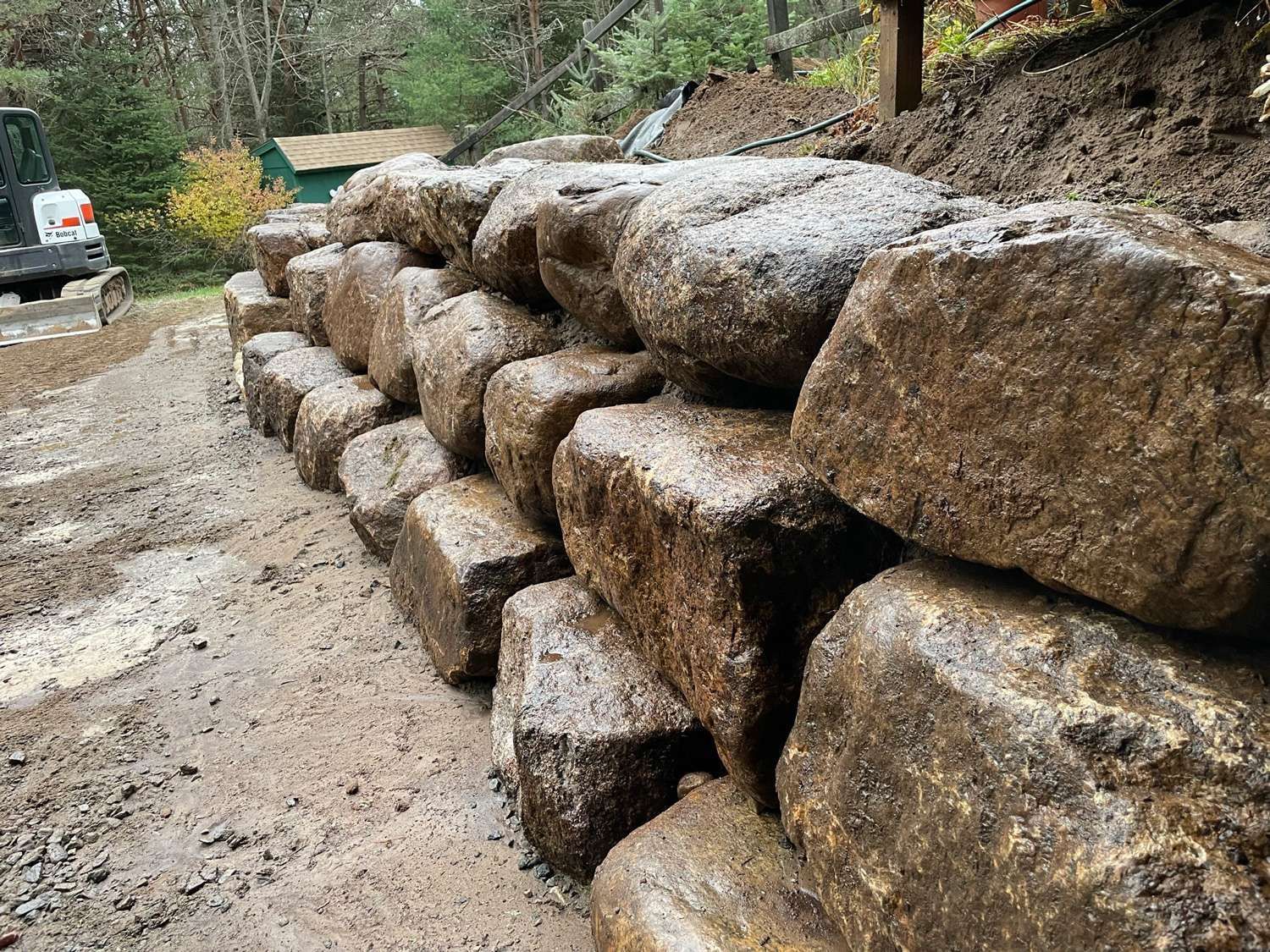 Stacked stone retaining wall beside a muddy dirt road in a wooded area