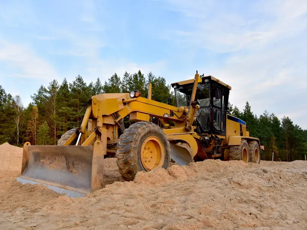 Yellow bulldozer leveling sandy soil in a forest clearing under a blue sky