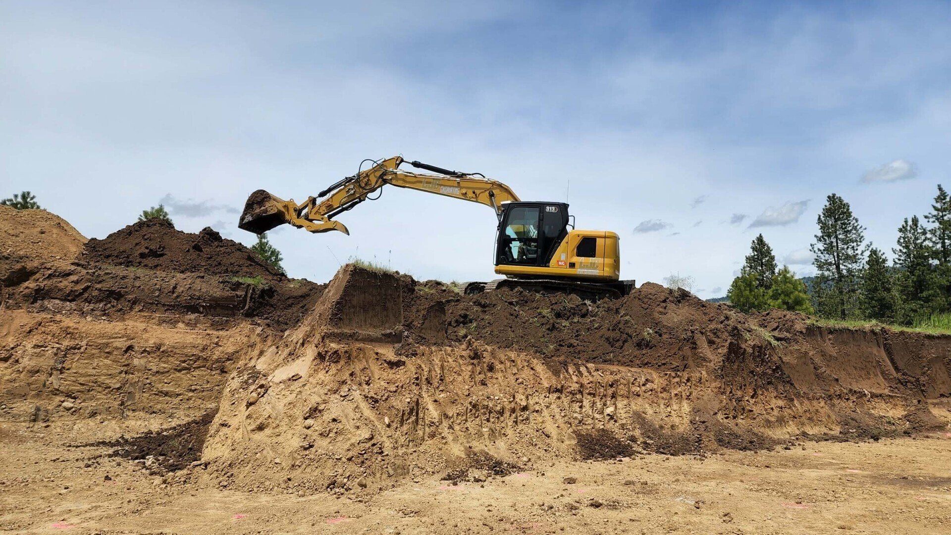 Yellow excavator digging a dirt mound at a construction site under a blue sky