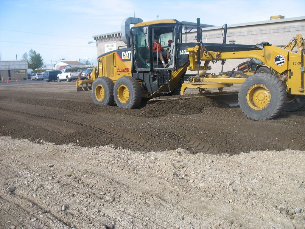 Yellow CAT road grader smoothing dirt at a construction site under a clear sky