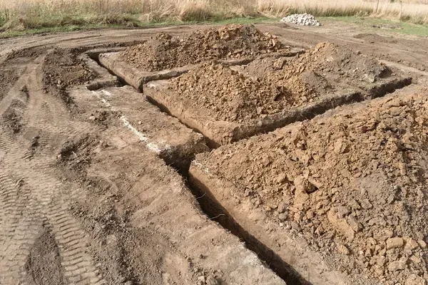 Freshly dug soil in rectangular plots on a dirt field, with tire tracks along the left side.