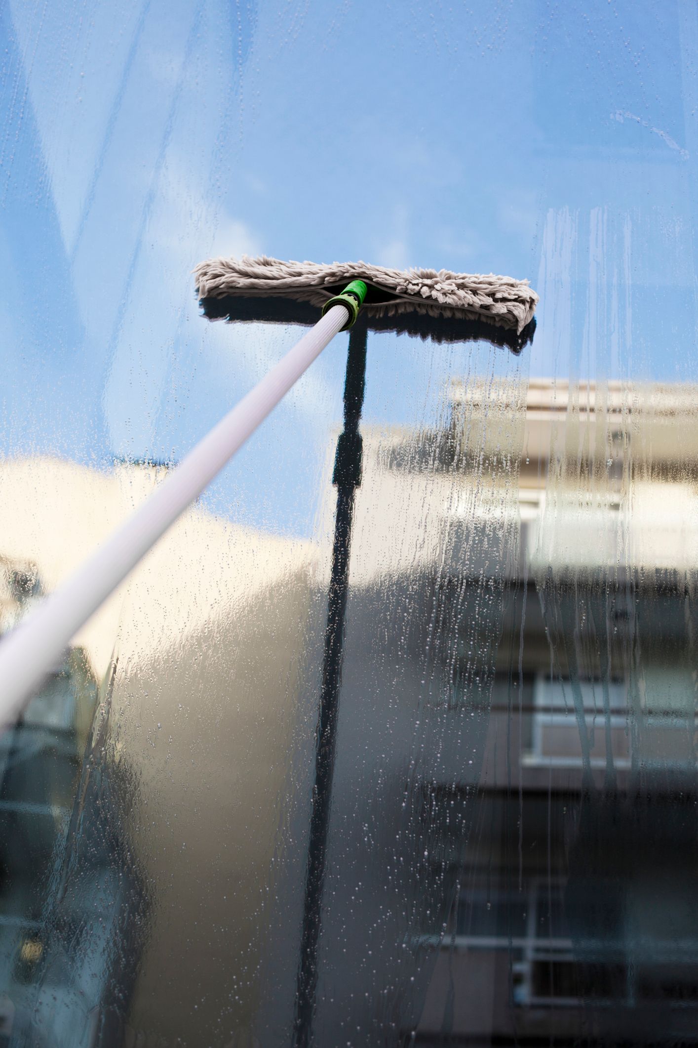 A person is cleaning a window with a mop on a pole.