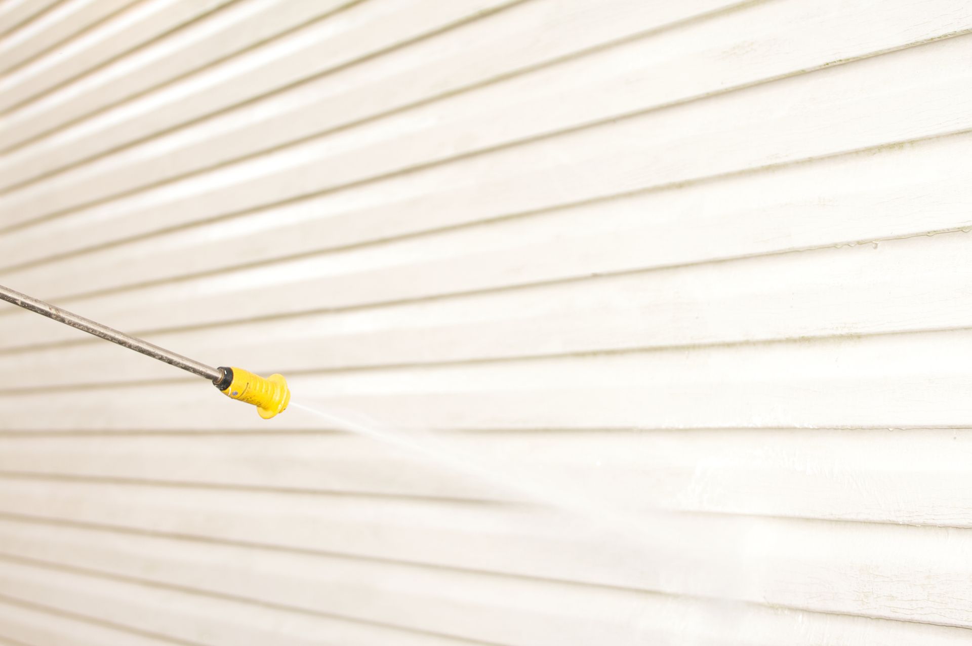 A person is cleaning a white siding with a high-pressure washer.