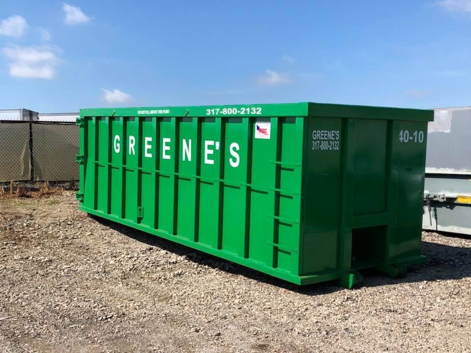 Green Greene's dumpster against a blue sky, on a gravel surface.