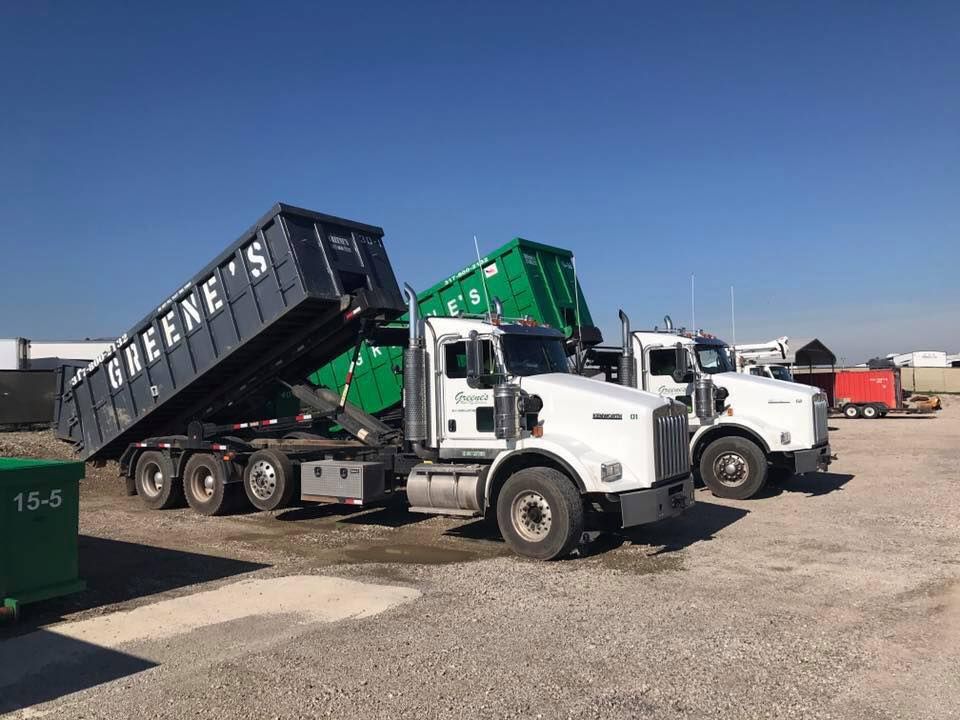 Two dump trucks with containers, one lifting, in a lot on a sunny day.