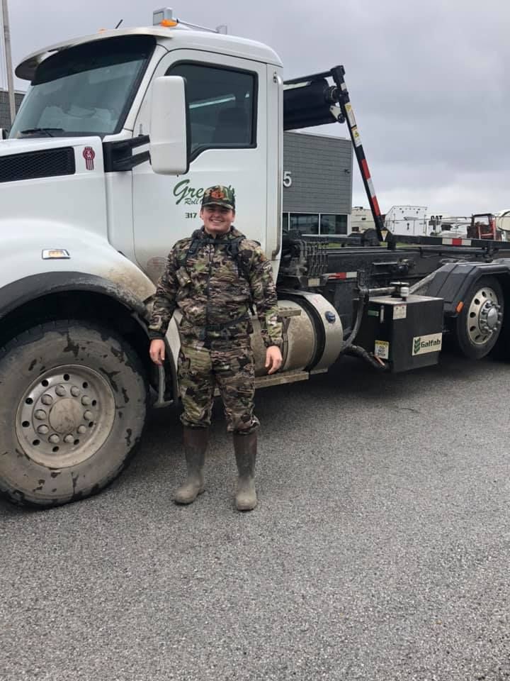 Person in camouflage standing next to a white industrial truck. Gray gravel lot. Person in camouflage standing next to a white industrial truck. Gray gravel lot.