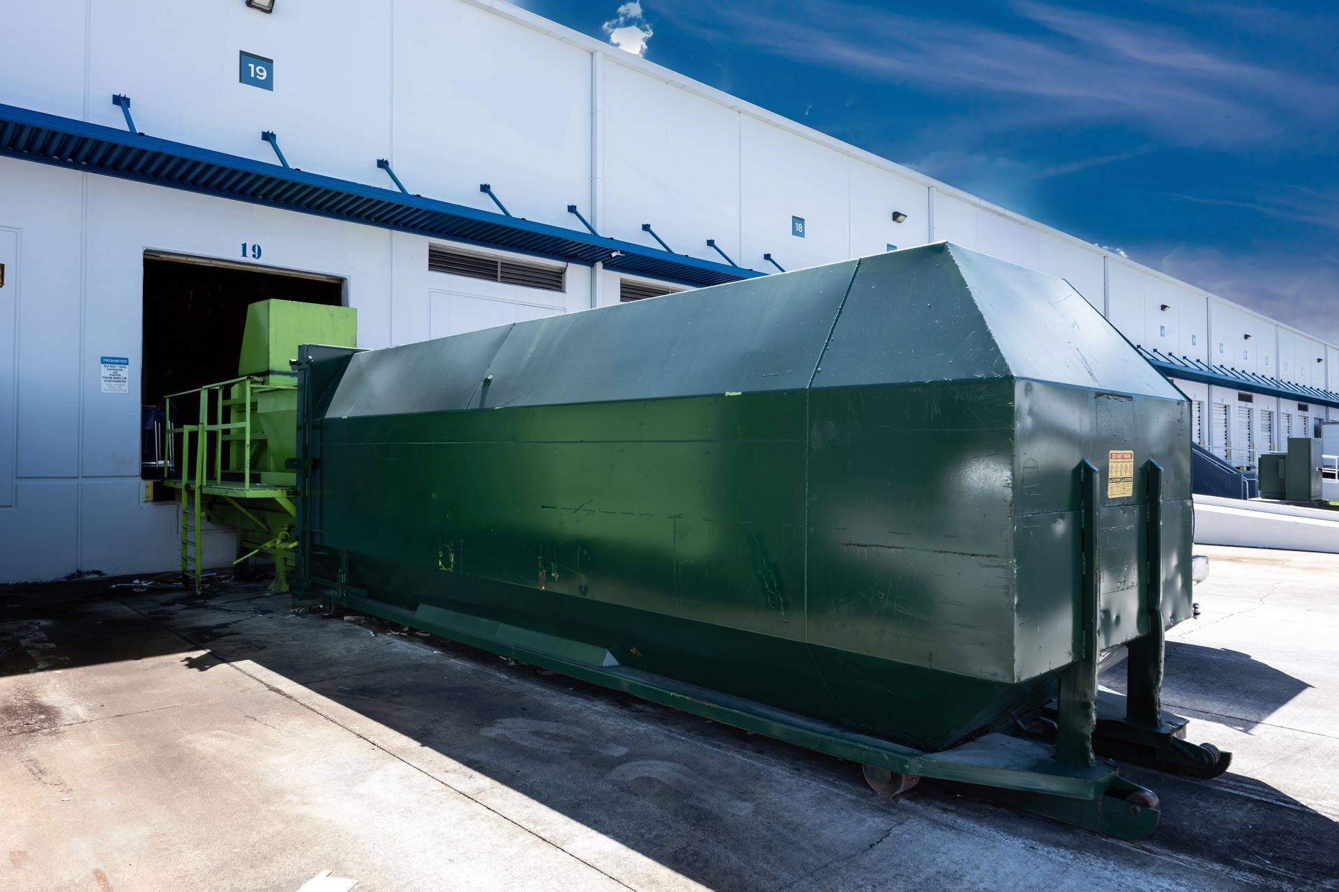 Green industrial waste compactor outside a loading dock. Green industrial waste compactor outside a loading dock.