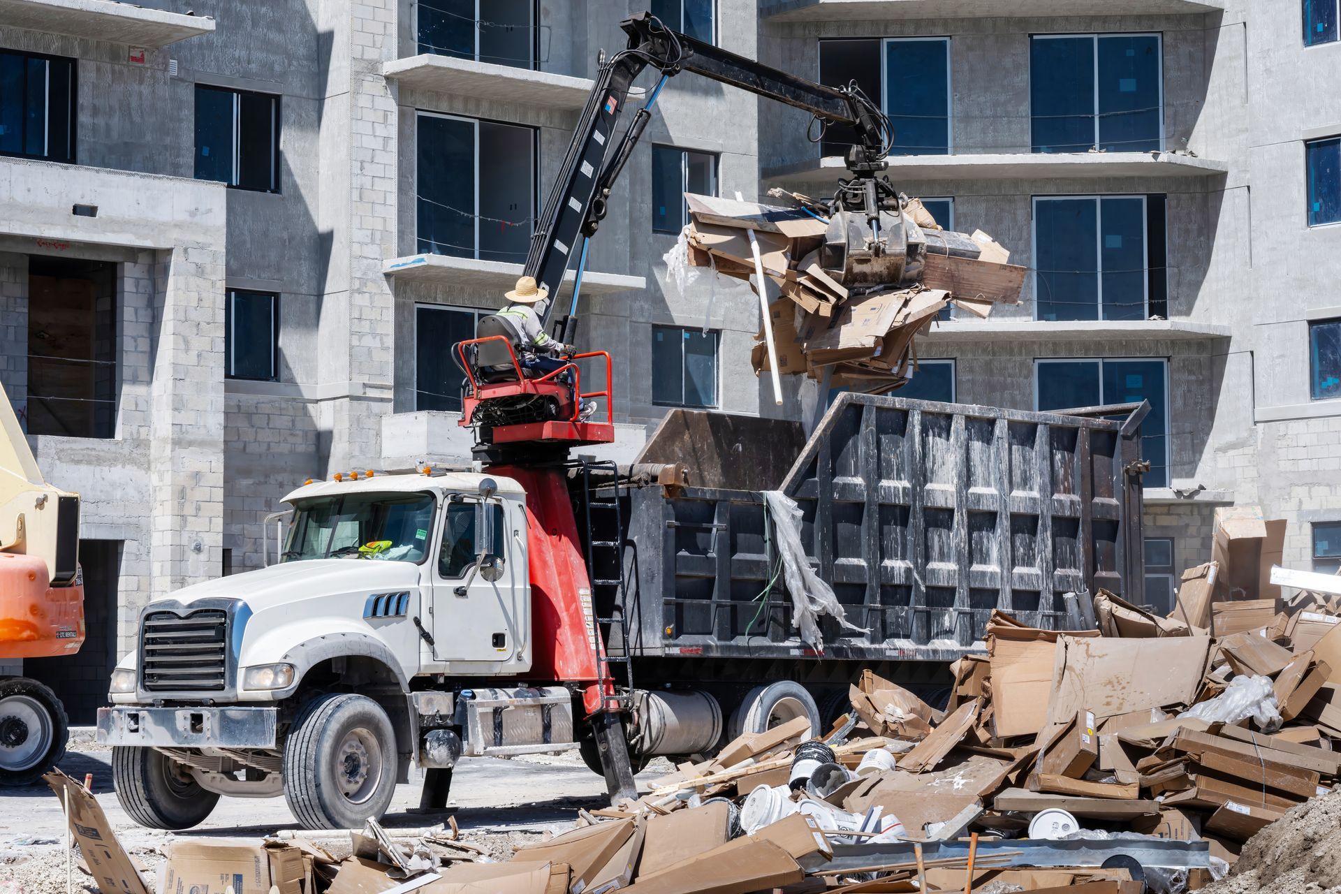 A construction truck loading debris from a building site with a mechanical arm. A construction truck loading debris from a building site with a mechanical arm.