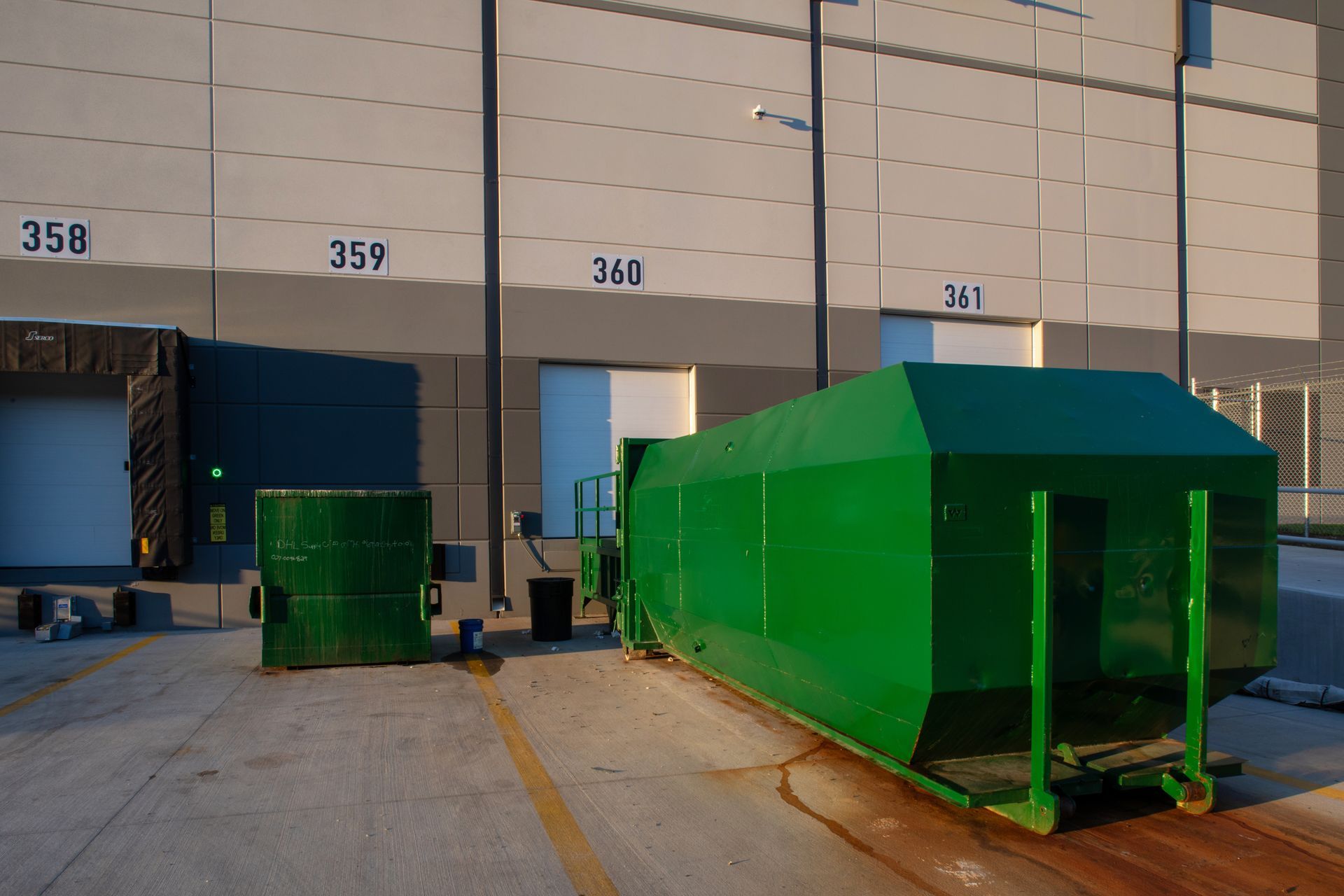 Orange industrial garbage bins, street setting, a green bin, and buildings in the background. Orange industrial garbage bins, street setting, a green bin, and buildings in the background.