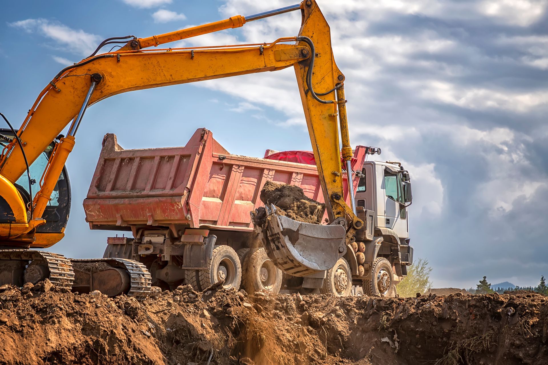 Yellow excavator loading dirt into a red dump truck at a construction site. Yellow excavator loading dirt into a red dump truck at a construction site.