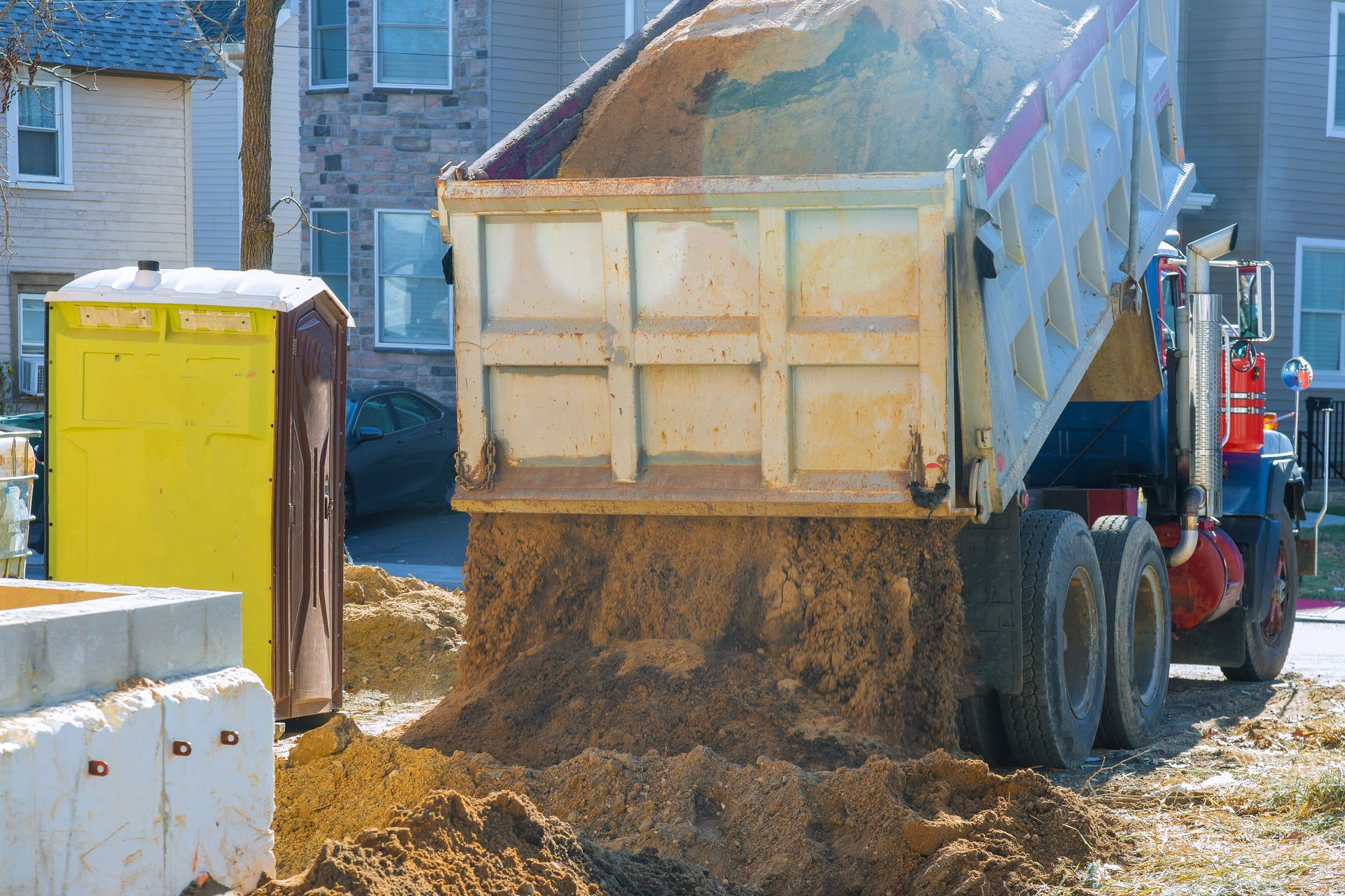 Dump truck unloading dirt near a yellow portable toilet and a concrete structure. Dump truck unloading dirt near a yellow portable toilet and a concrete structure.