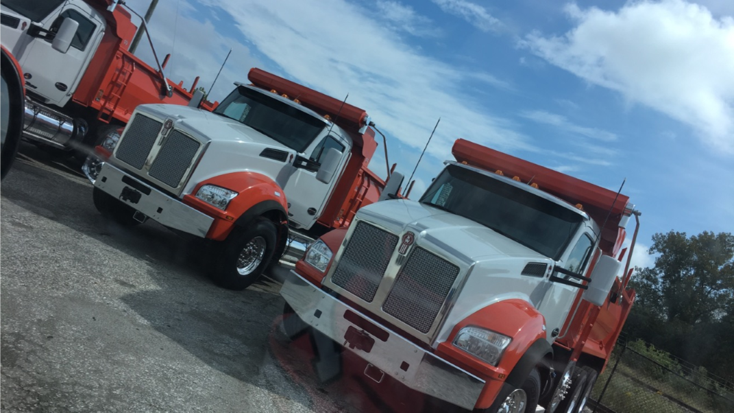 Three white semi-trucks parked inside a garage, next to support columns. Three white semi-trucks parked inside a garage, next to support columns.