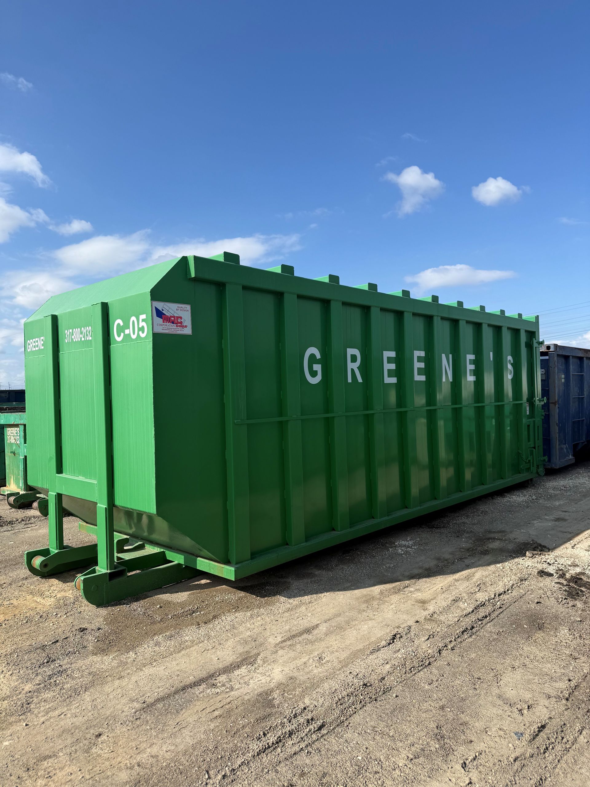 Three dumpsters, blue and green, next to a white car parked under a 'P' sign. Buildings with green roofs in background. Three dumpsters, blue and green, next to a white car parked under a 'P' sign. Buildings with green roofs in background.
