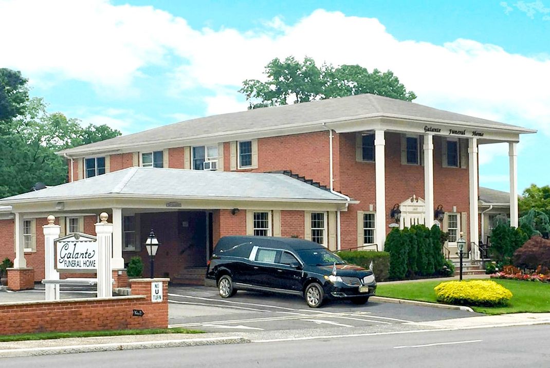 Brick two-story building with a covered entrance and black SUV parked outside under a bright sky