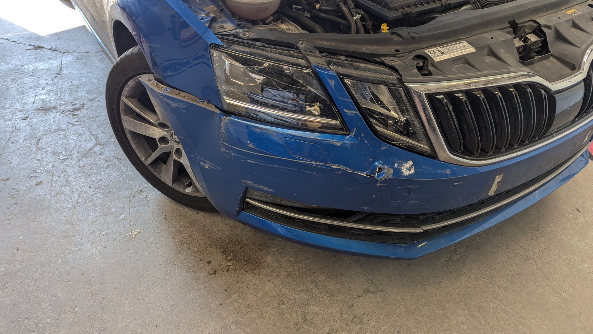 Blue SUV with front-end damage and scratches in a garage or repair shop