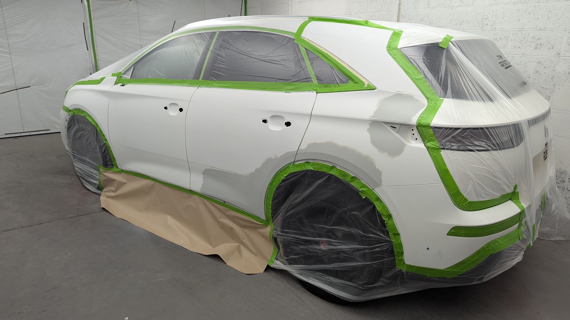 White sedan masked with green tape and protective coverings, parked in a garage or auto body shop