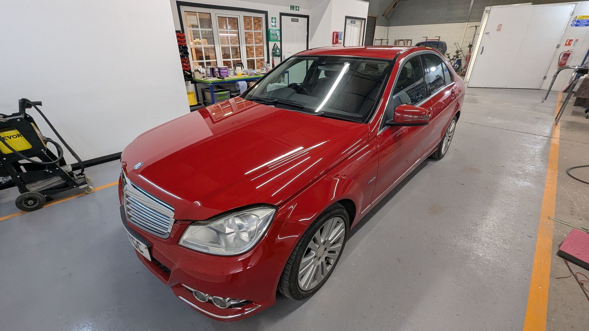 Red sedan parked inside a garage or workshop, viewed from the front-left side.