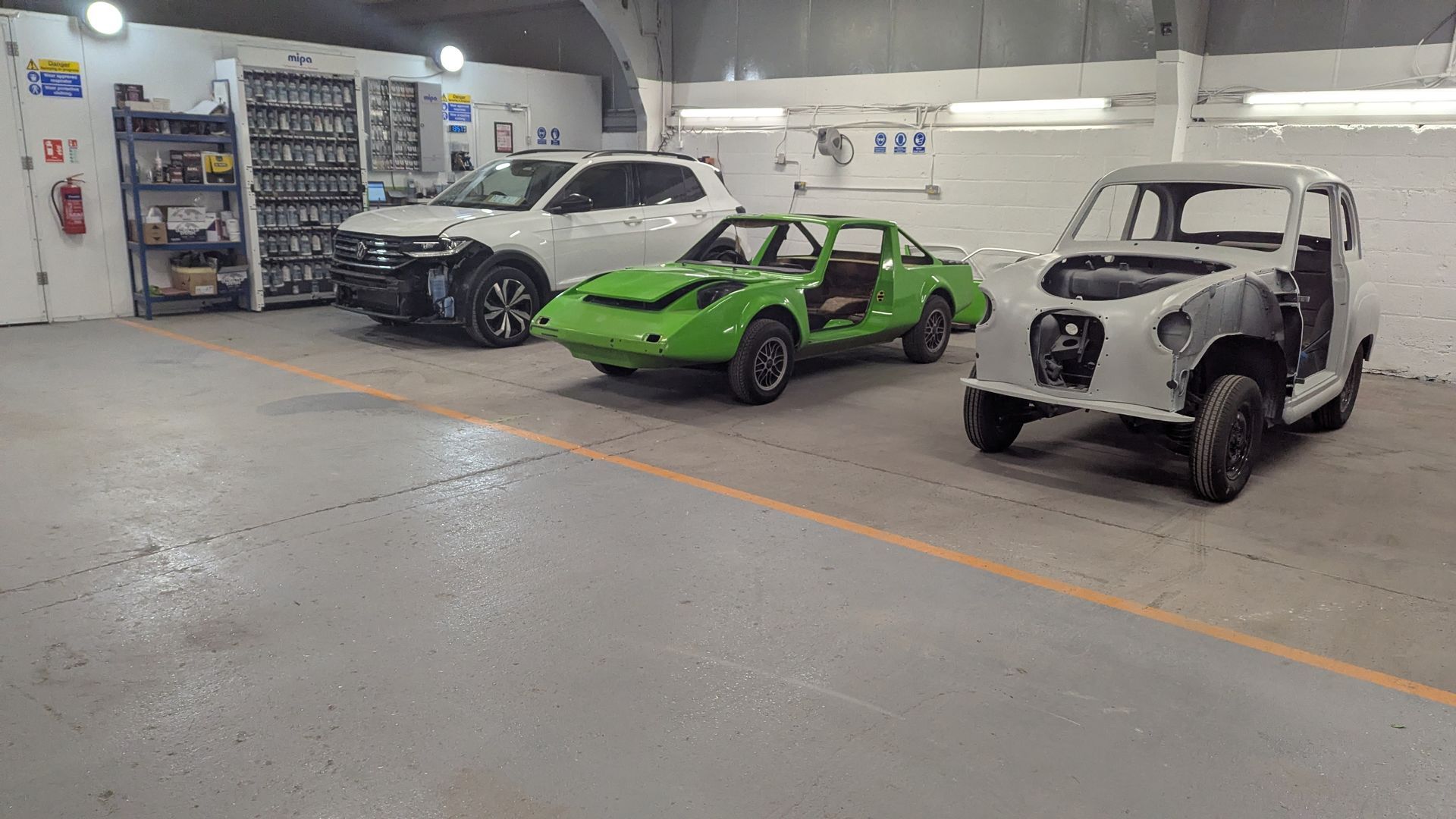 Three cars in a garage: white sedan, bright green sports car, and white vintage truck