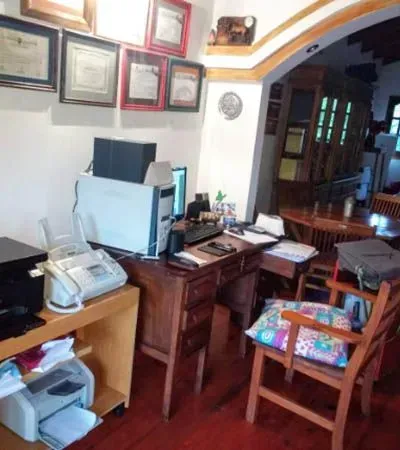 Despacho en casa con escritorio, ordenador, impresora, certificados enmarcados y una silla de madera.