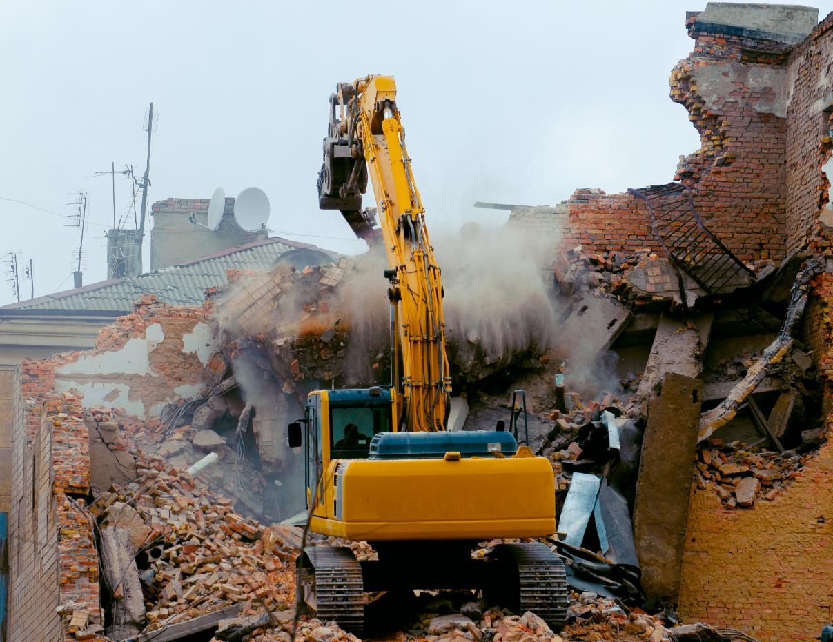 A Yellow Excavator is Demolishing a Brick Building — Husky Demolition In Port Stephens, NSW